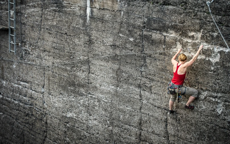 woman in red shirt climbing up the side of a tall wall