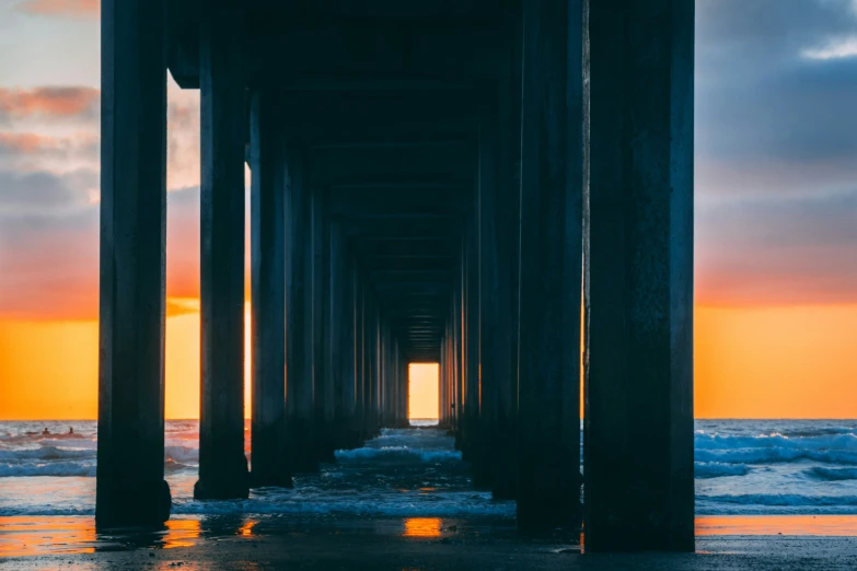 an orange and blue sunset behind the ocean under a pier