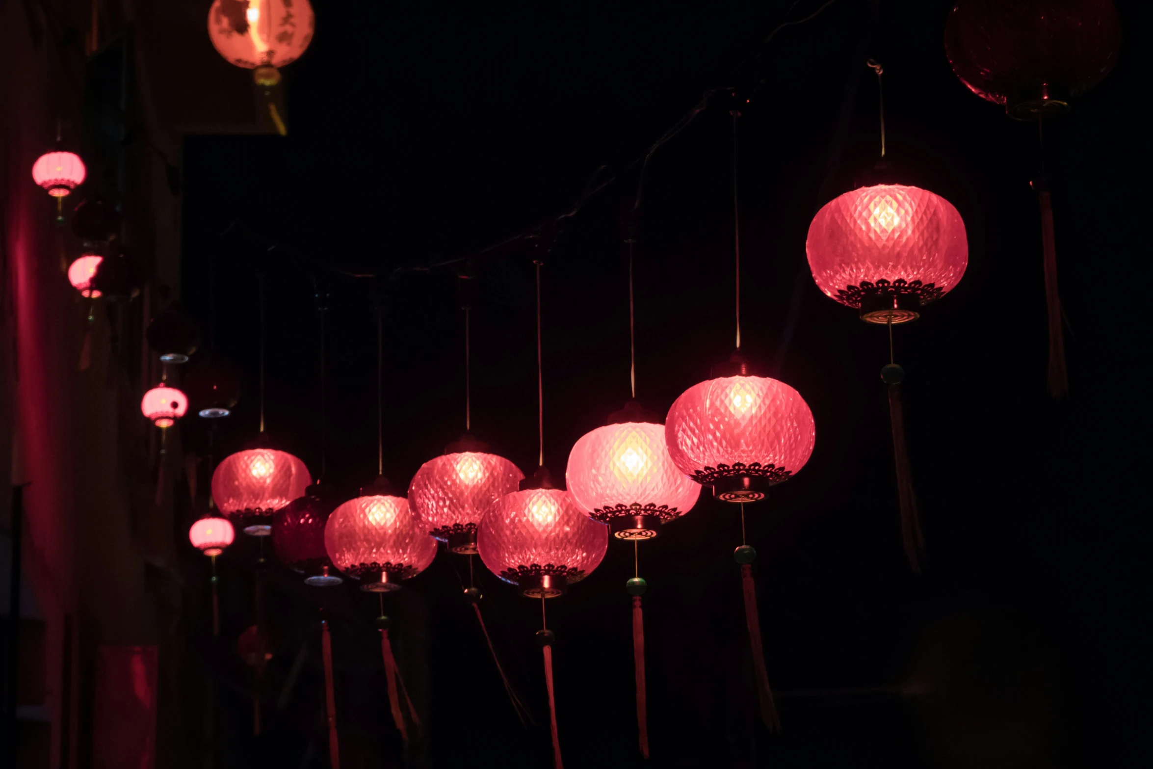 many lanterns lit up in the dark, with a wall in the background