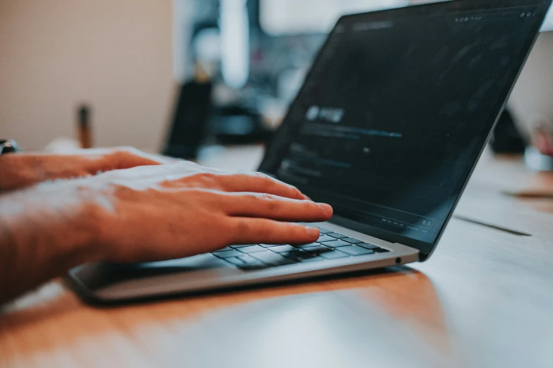 the hand on top of the laptop is pressing the keys on it