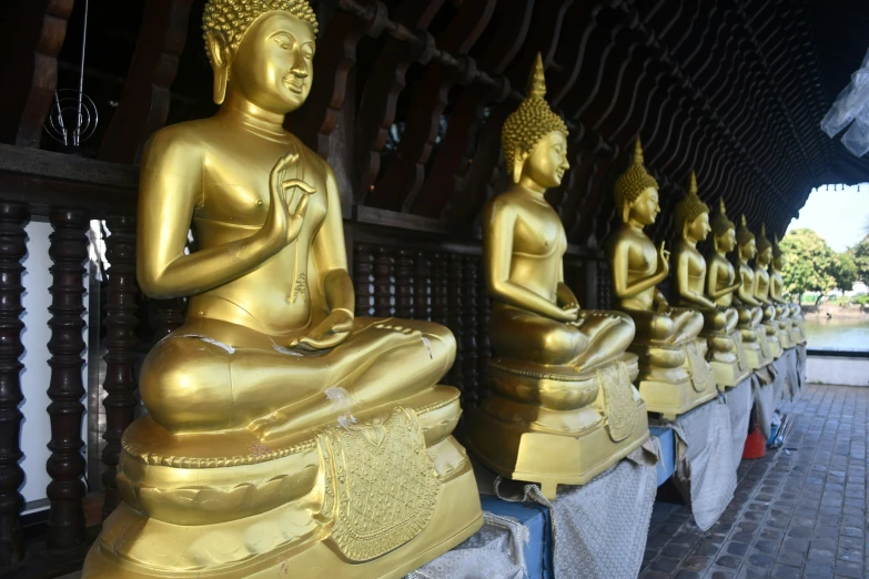 four large gold buddhas sitting on benches, one on the ground