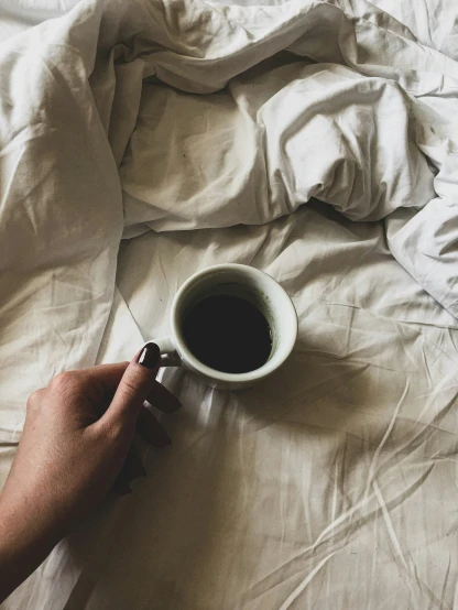 someone that is holding a cup of coffee on a bed