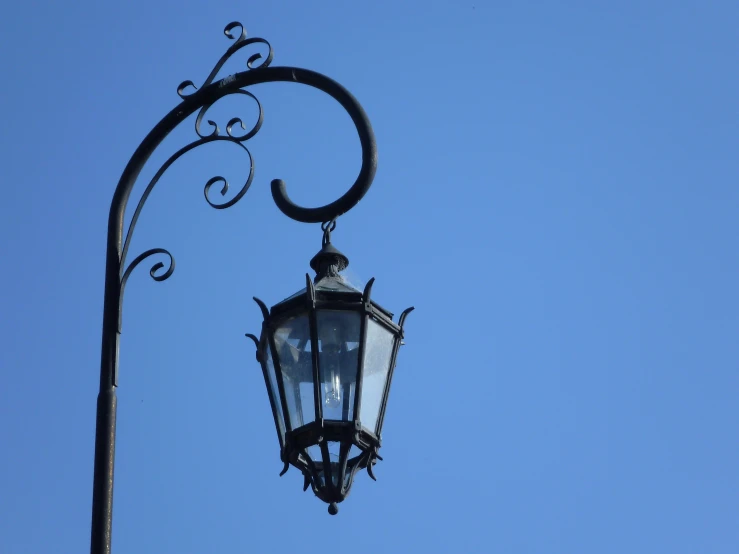 an old fashioned street light with curved metal design against a blue sky