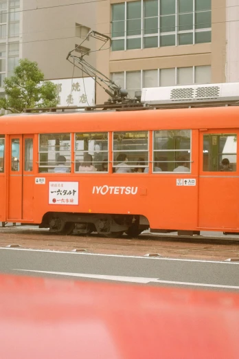 a bright orange tram passes by a large city building