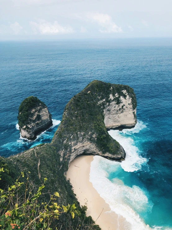 a beach with two large cliffs in the middle and blue water