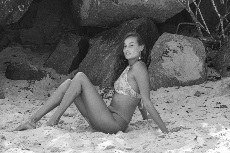 a woman laying in the sand next to rocks and water