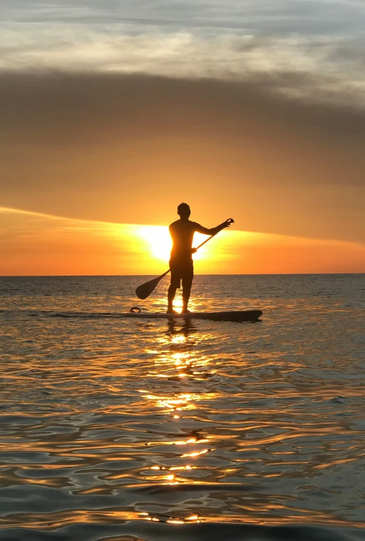 a person paddle boarding in the water during sunset