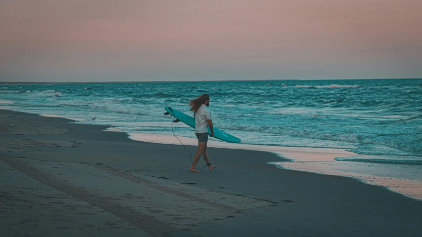 a woman carrying a surfboard walks along the beach
