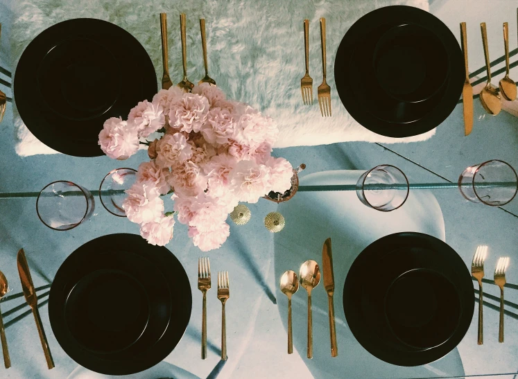 the place setting is all decorated with gold cutlers, black plates and pink flowers