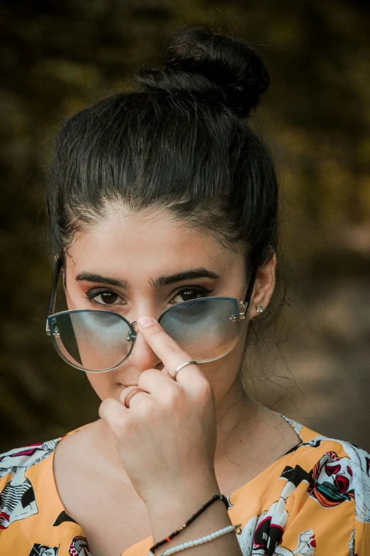 a girl in sunglasses wearing a colorful shirt and holding her hand to her face