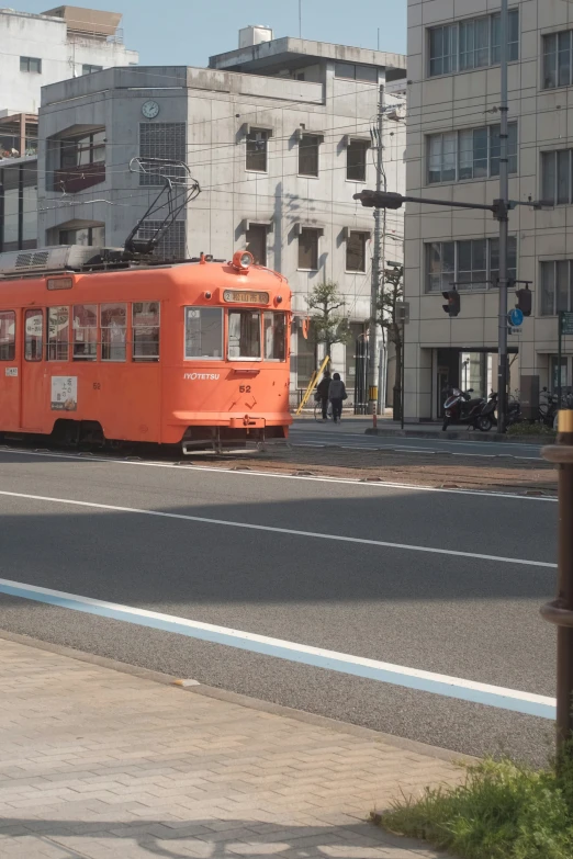 an orange trolley going down the tracks next to a street