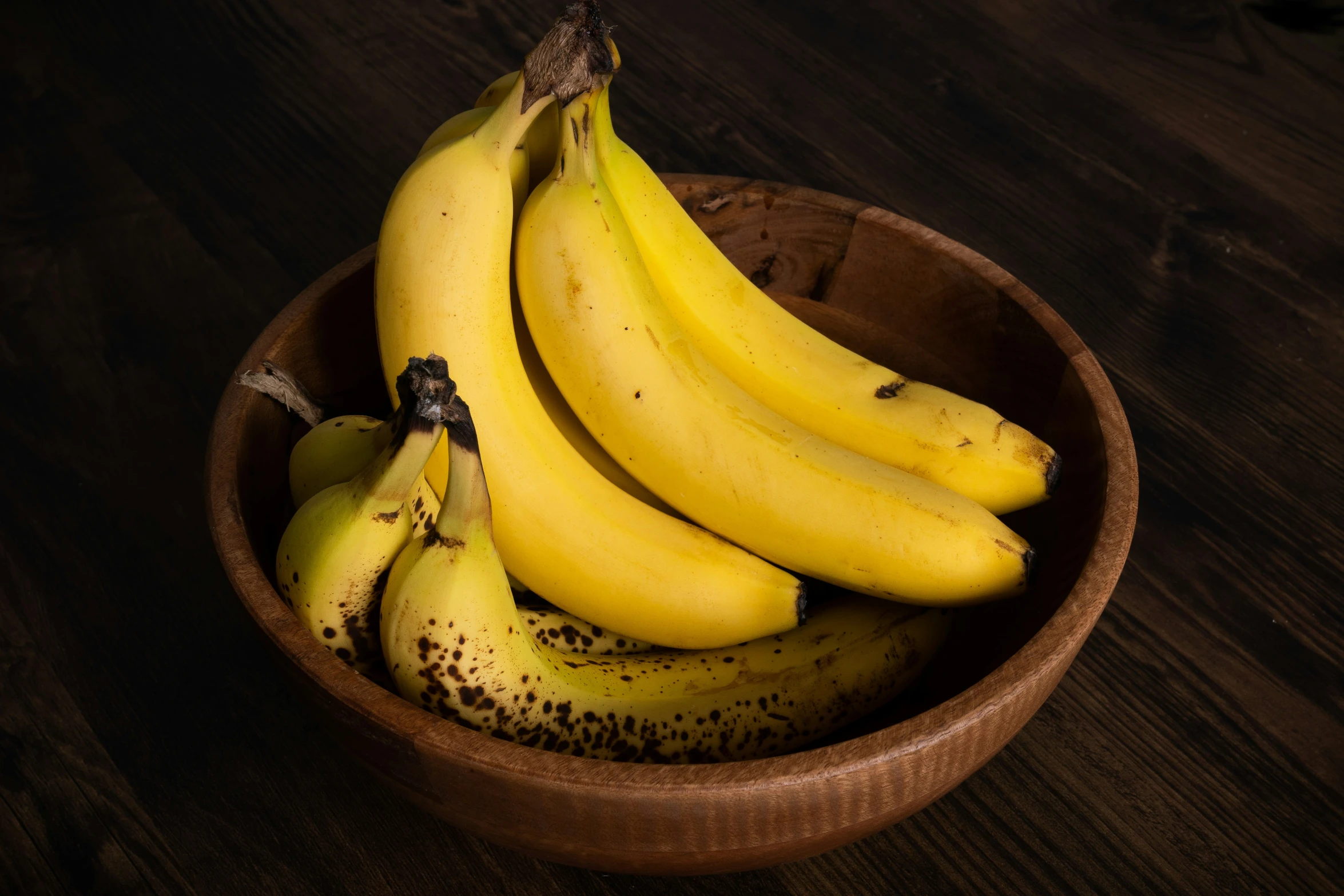 ripe bananas are piled in a wooden bowl