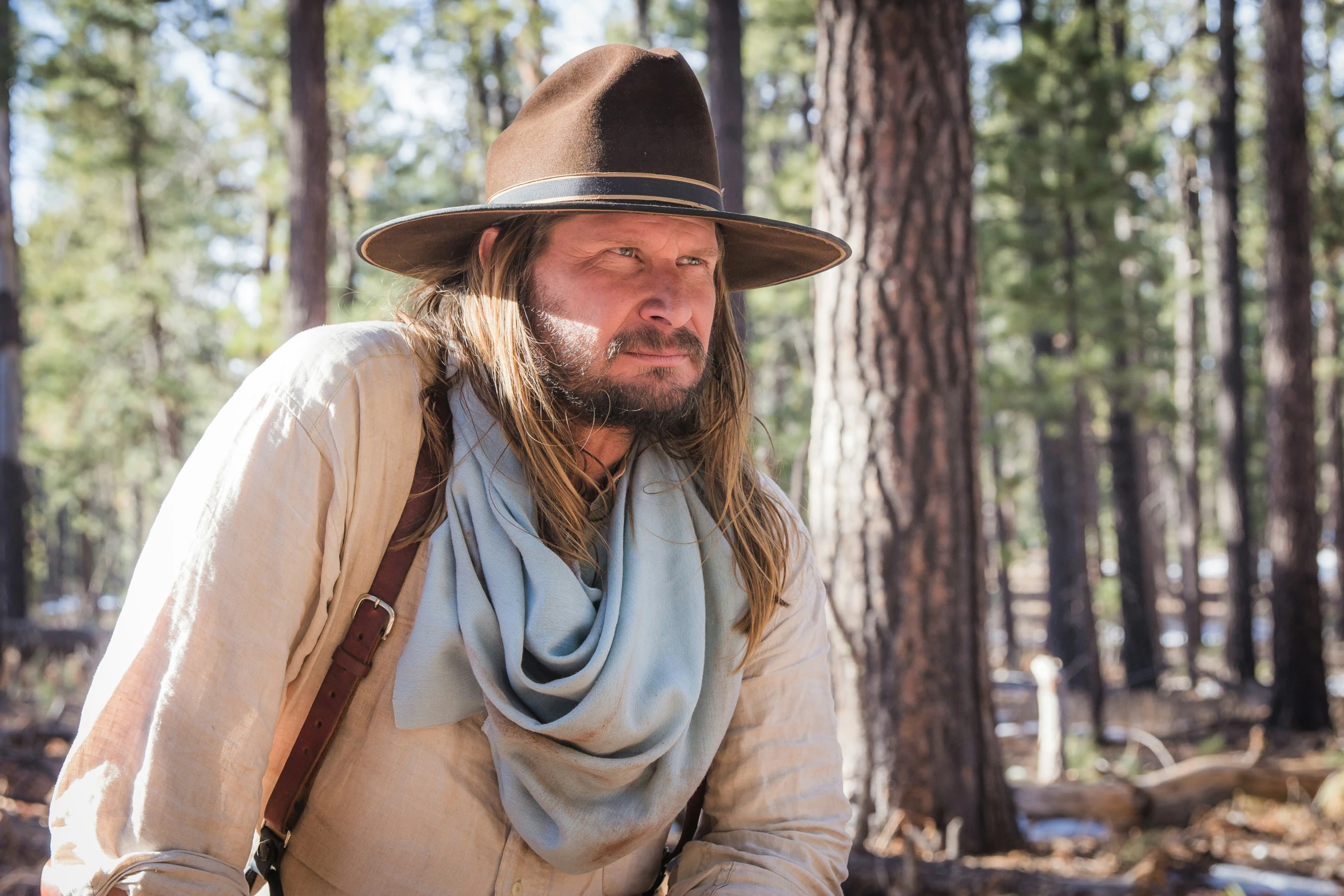 a man wearing a hat and scarf is kneeling in the woods