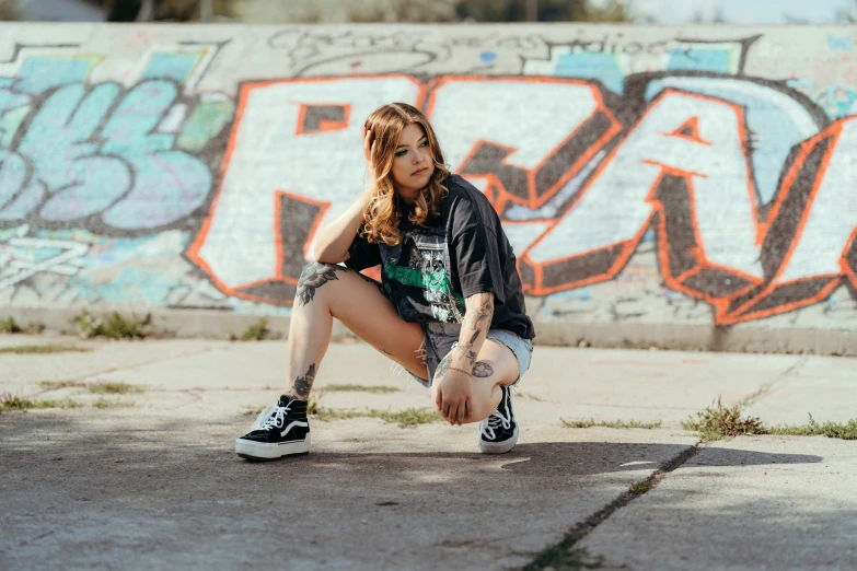 a young woman poses next to a graffiti covered wall