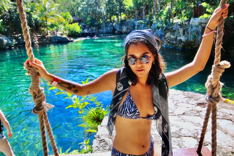 a woman with sunglasses and a bandana on standing on swings in front of a pool