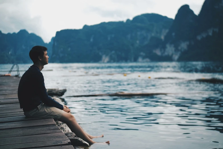 a man sits on a dock near the water