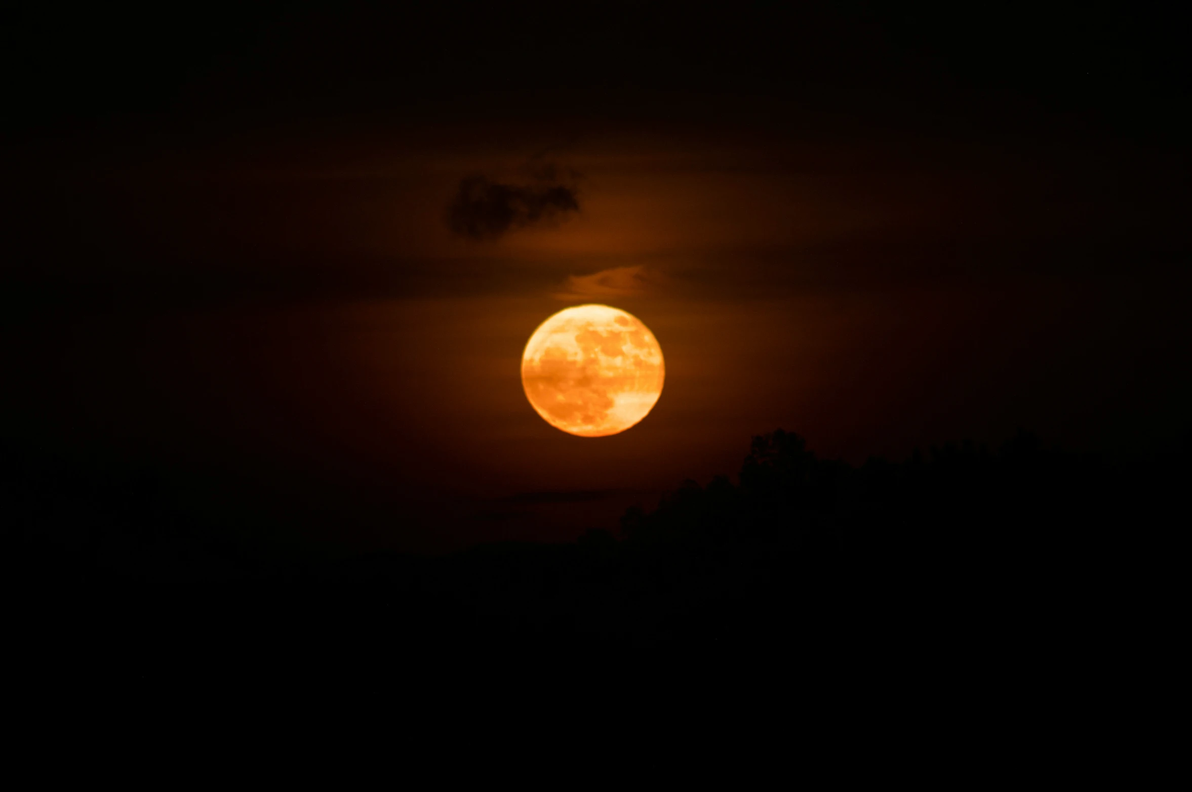 the moon shining through clouds over the tree tops