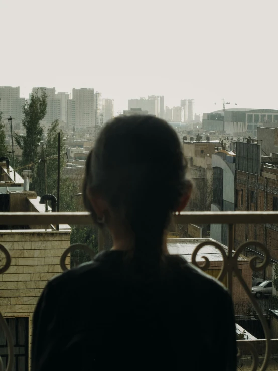the back of a woman standing at a window with a view of city