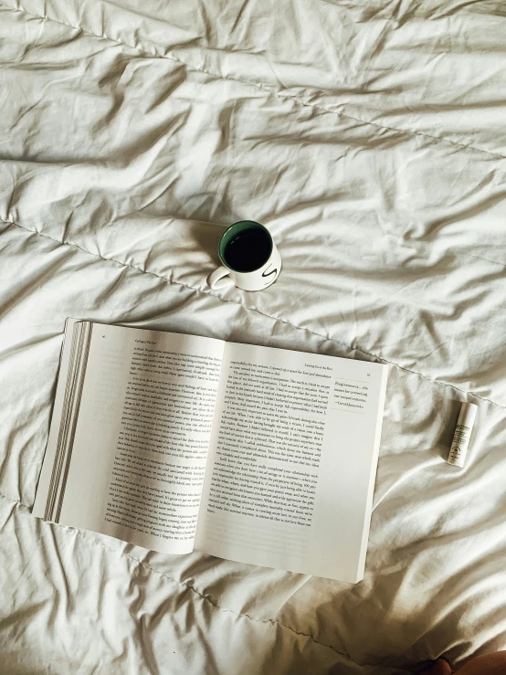 book and cup on a bed with white sheets