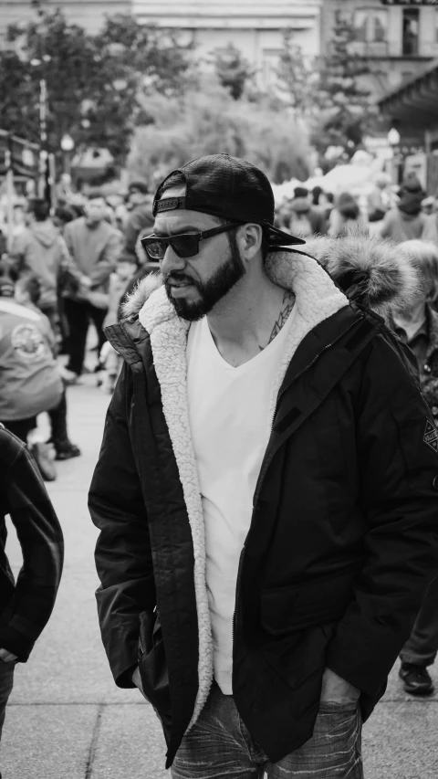 a bearded young man is walking with people standing around