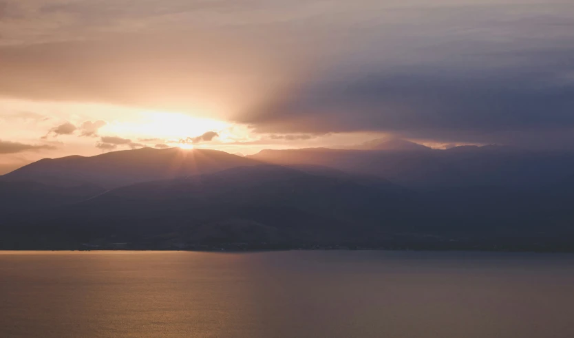 the sun is shining through clouds over the water