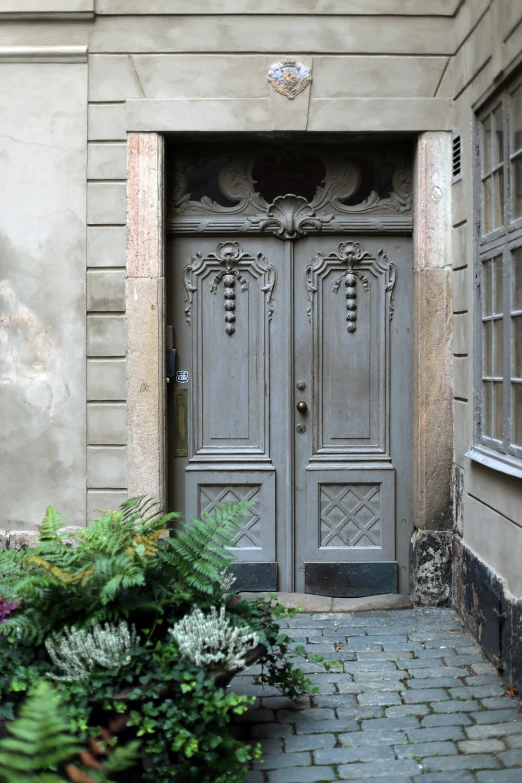 a door that is grey in color surrounded by flowers and greenery