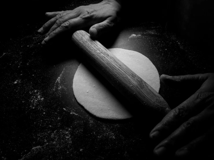 two hands hold a rolling pin over a dough