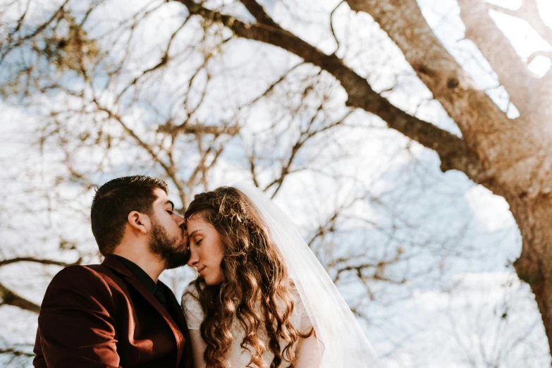 a bride and groom posing for a wedding po under a large tree