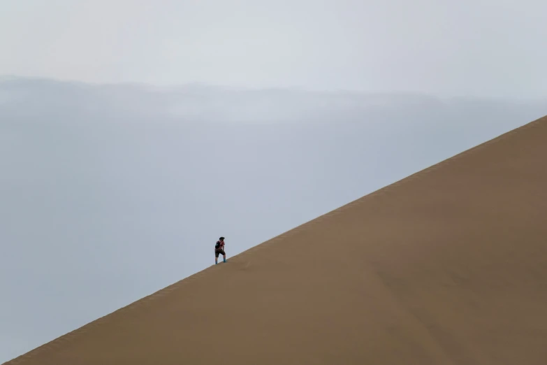 a man walking up a sand dune to the sky