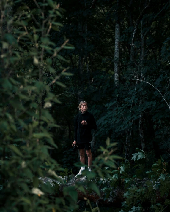a woman walking through a forest next to a tree