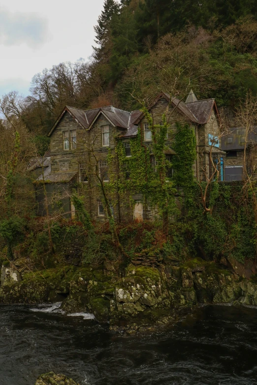 an old house near the water with ivy growing up it