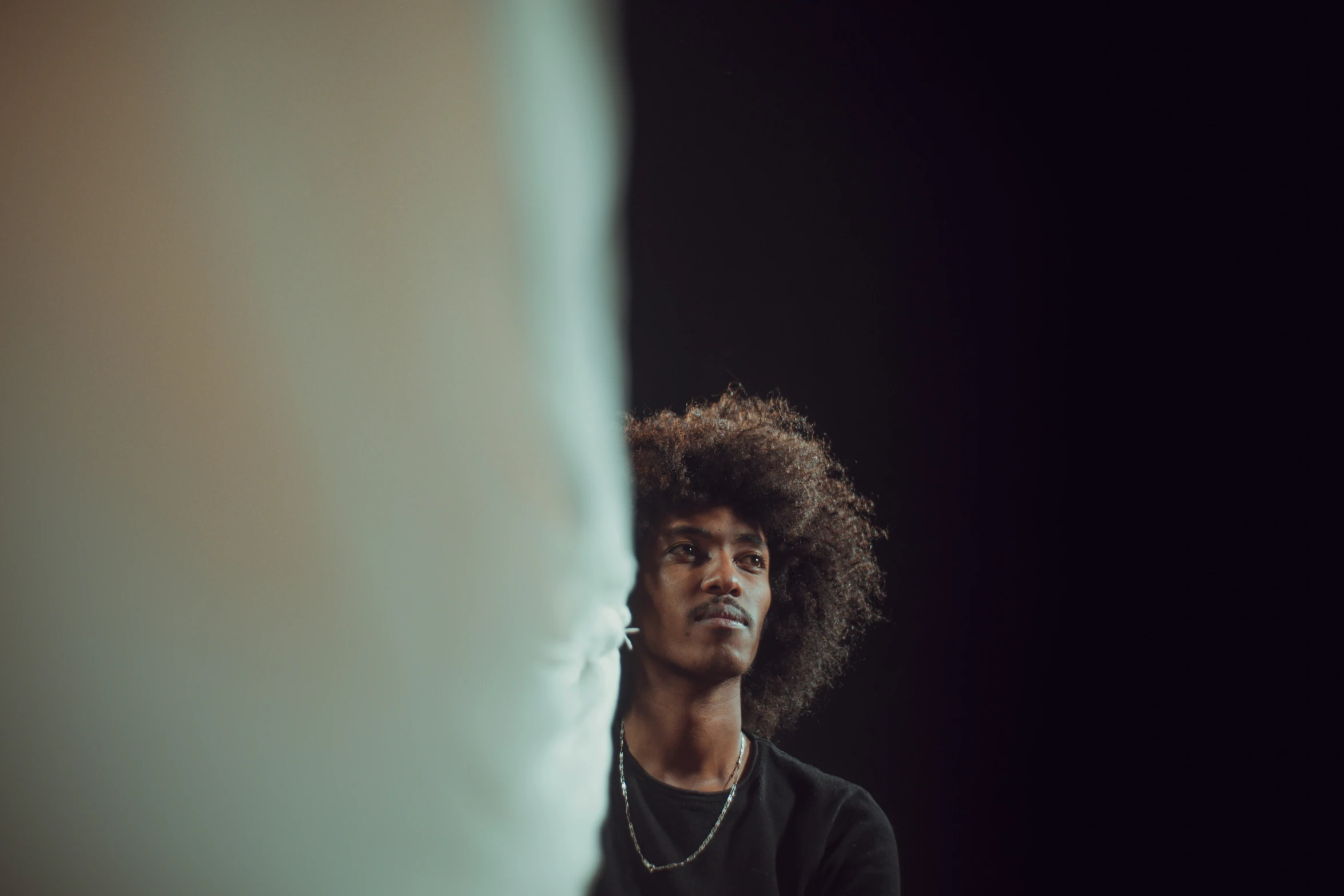 man with black outfit wearing earring and looking at his reflection in a mirror