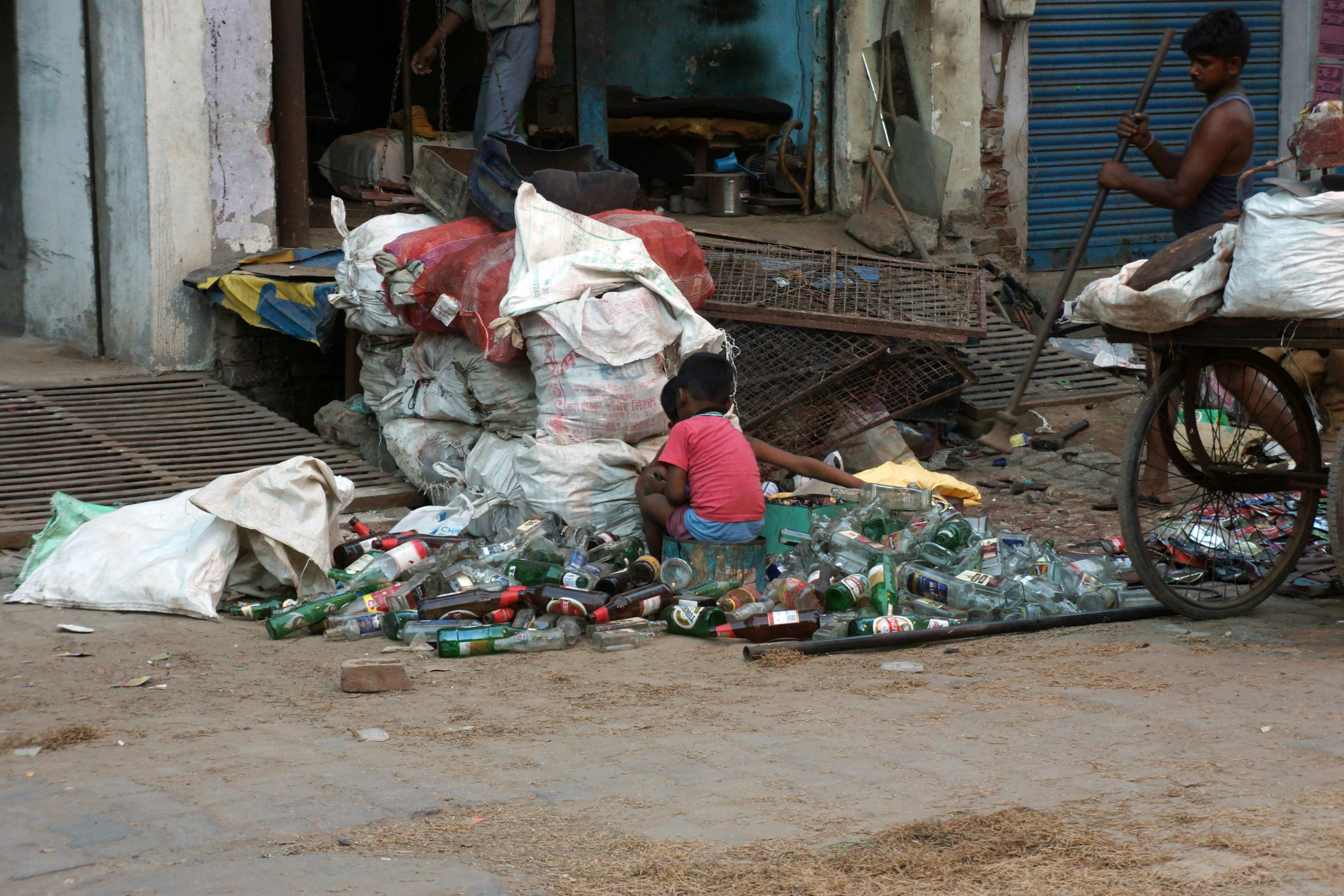 a person sitting on the street in front of a pile of plastic bottles