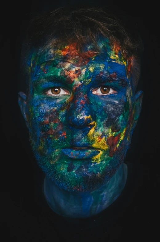 a man is covered with colorful powder, and has his face painted bright