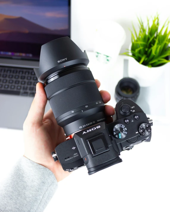 a person holding a camera and a laptop on a desk