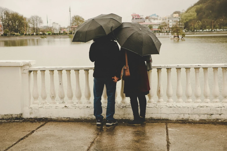 two people stand under umbrellas with their backs turned