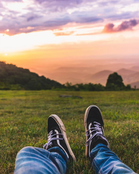 a person with their feet up in the grass looking at the mountains