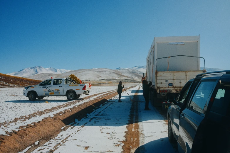 the two men are standing on the road beside a truck