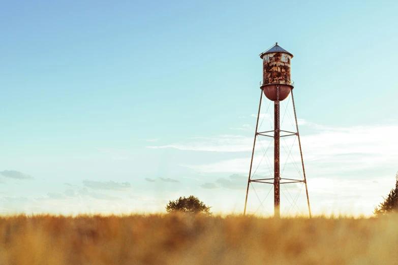 an abandoned water tower standing in the middle of a dry grass field
