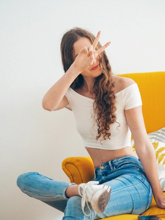 a girl wearing a crop top sits on the couch with her hand over her head