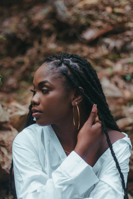 the side view of a black woman with dreadlocks in a white shirt outdoors