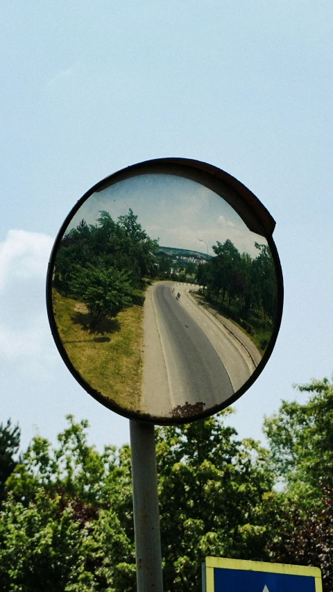 a rear view mirror reflecting the road next to trees