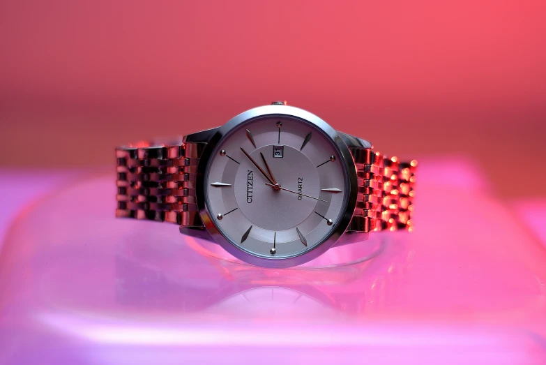 a watch sits atop a pink surface and is illuminated