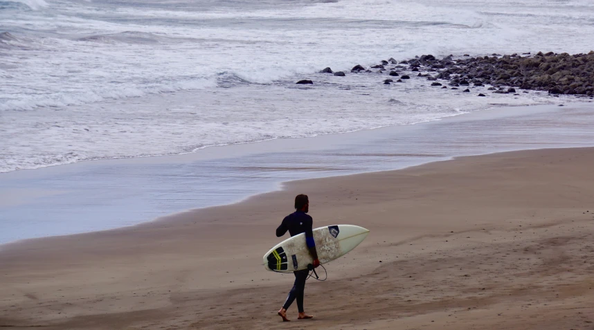 a person in a wet suit carries a surfboard toward the ocean