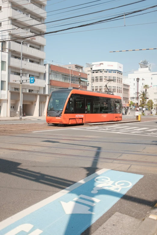 a bright orange train going down a street near tall buildings