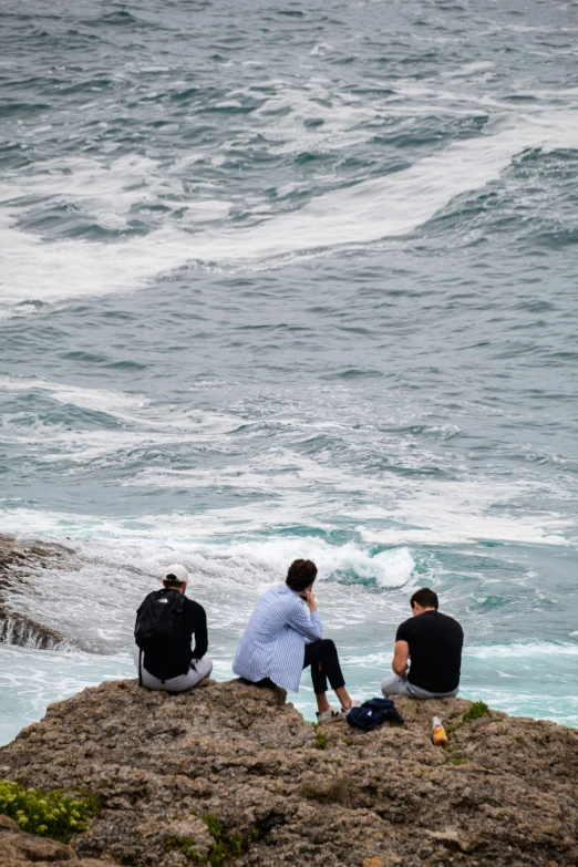 three people sitting on a rock next to the ocean