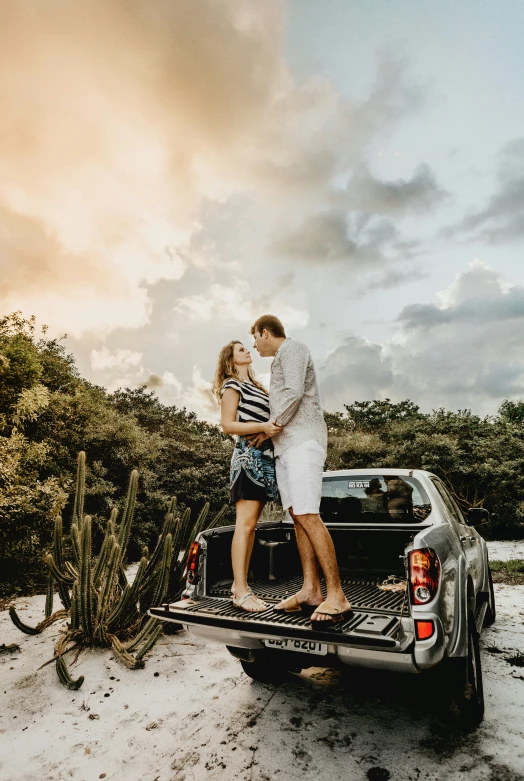 a couple cuddles on the back of a truck as the sun goes down in a desert