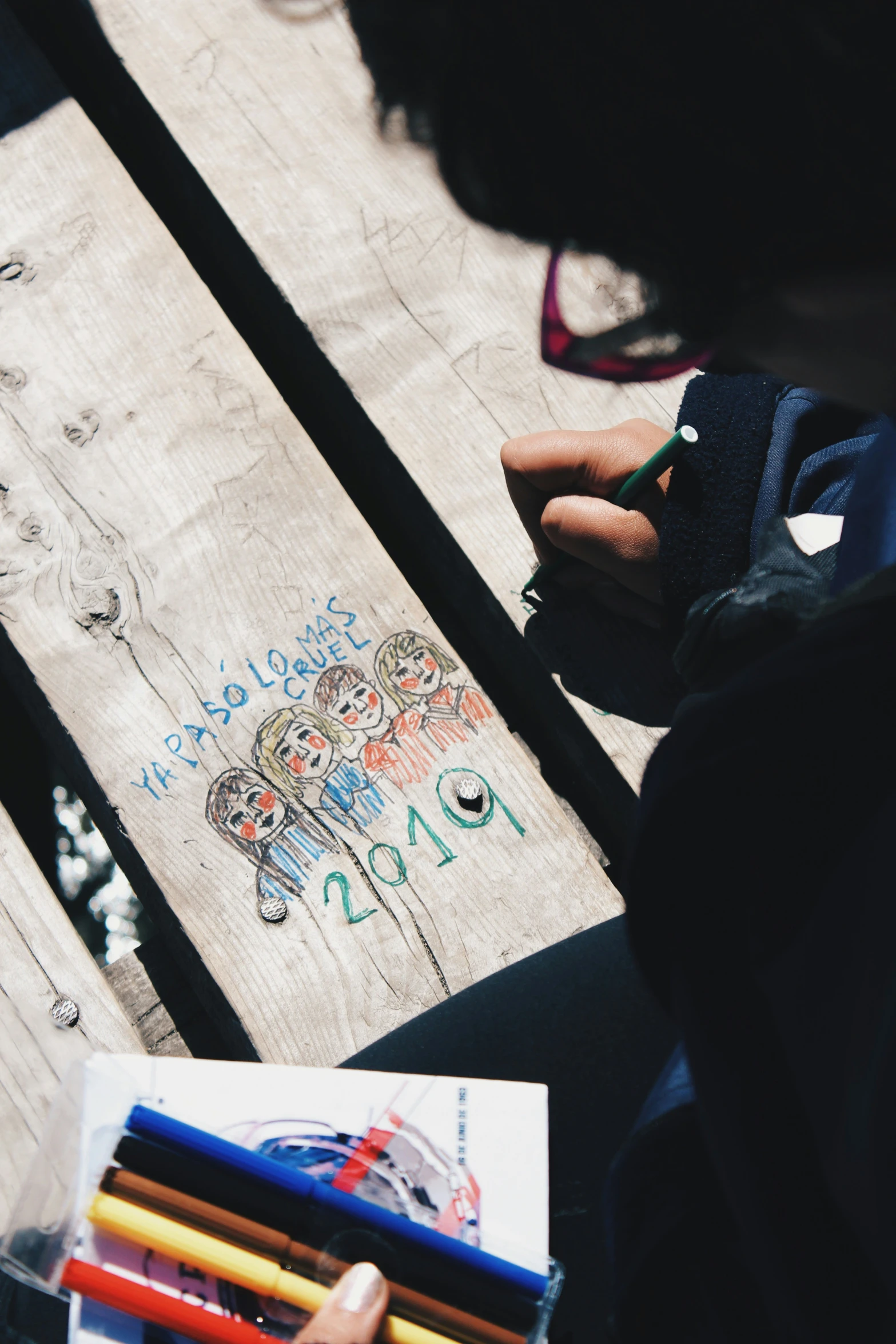 a woman's left hand holding a pair of crayons and a pencil