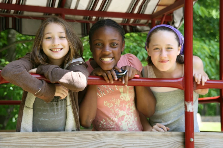 three smiling girls standing behind a metal rod