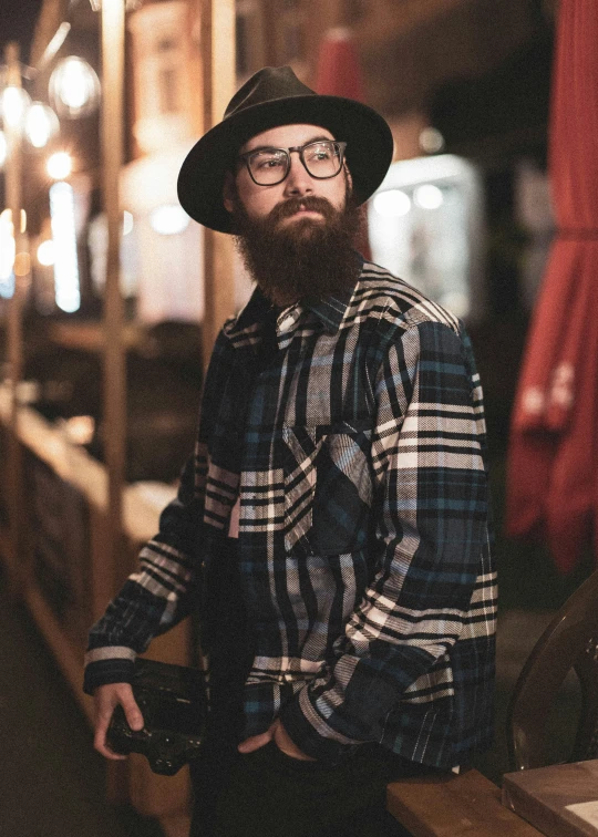 a man standing with his hands in his pockets wearing a hat and glasses